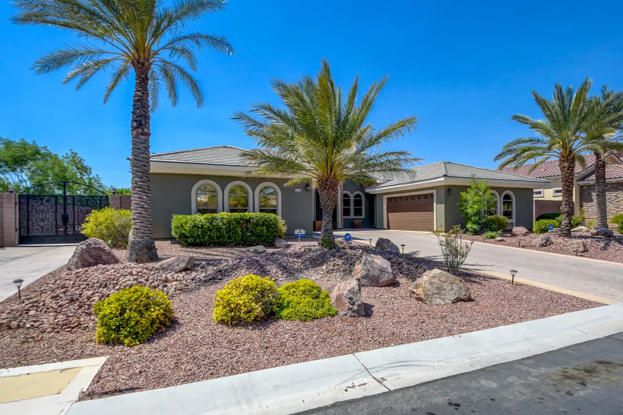 Front elevation of the one-story stucco home with a tile roof, palms and desert landscaping
