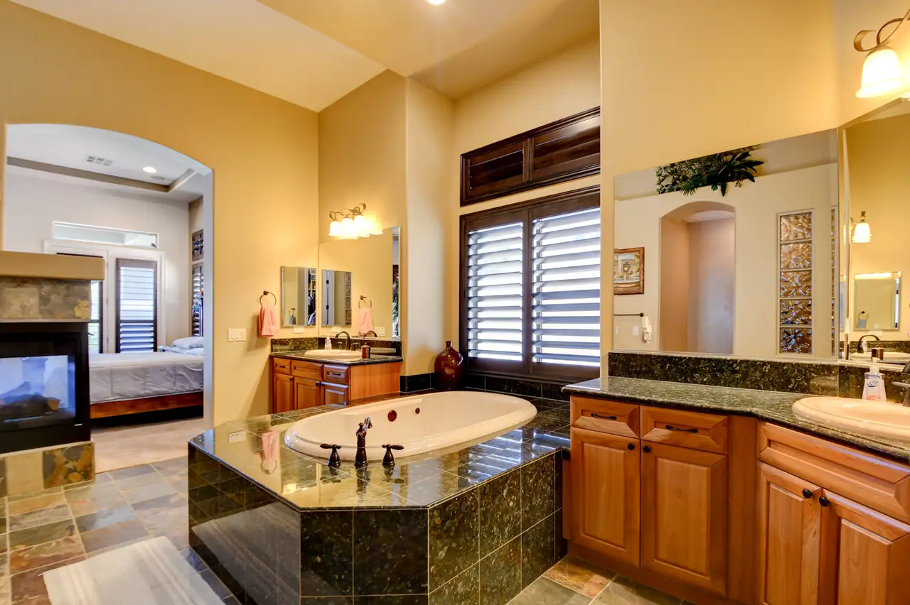 Primary bath tub set in dark granite with the two-sided fireplace beyond